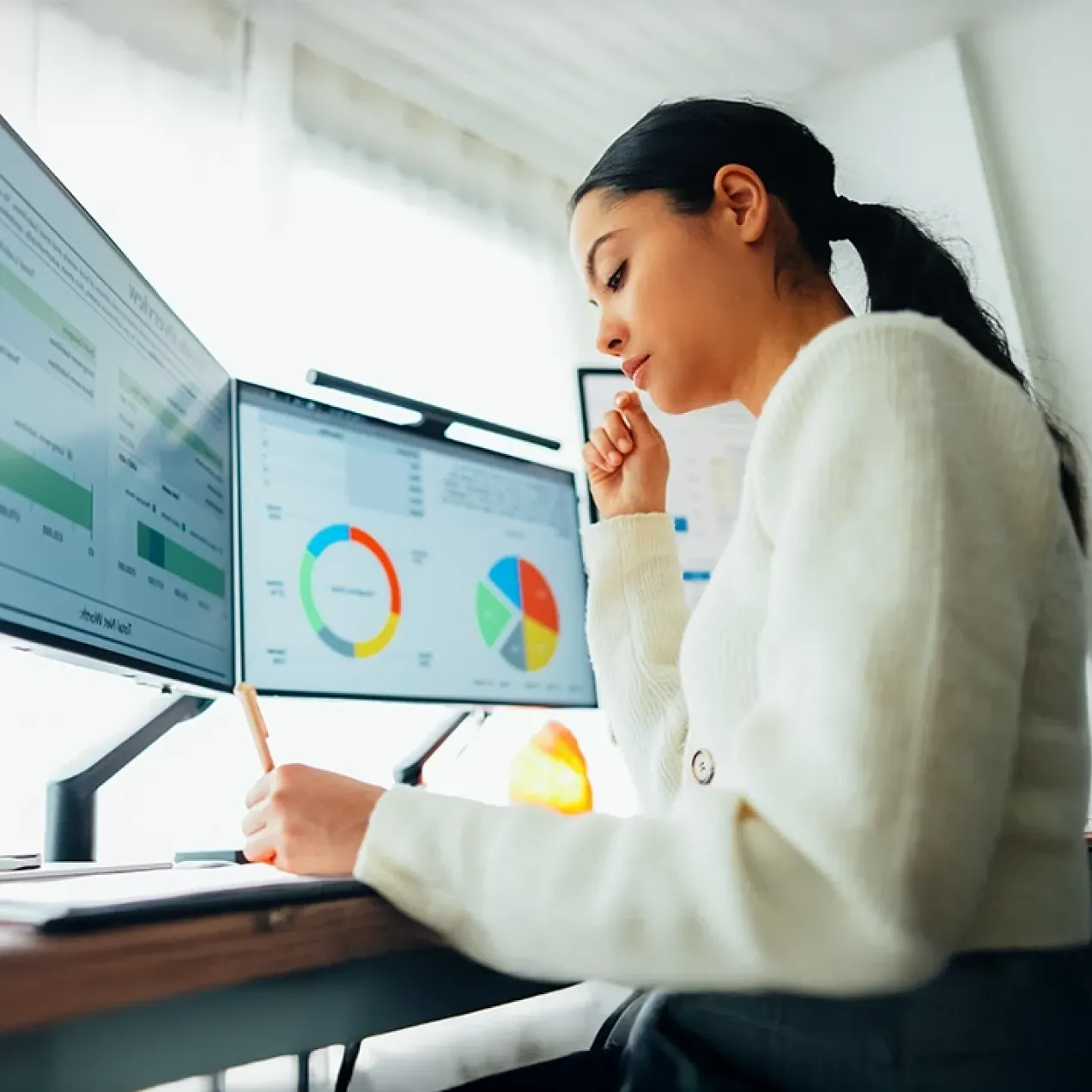 A professional woman analyzes data on dual monitors, representing the skills and expertise gained through Herzing University’s MBA in Business Analytics program.